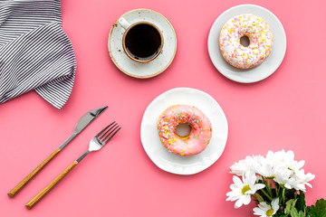 woman desk with flowers, coffee and donuts for breakfast in spring desing pink background flat lay