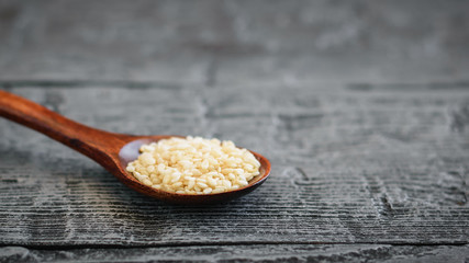 Sesame seeds in a spoon of dark wood on a dark table.