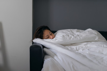 Asian woman sleeping on black leather sofa in white blanket