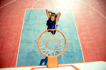 Young man jumping and making a fantastic slam dunk playing streetball, basketball. Urban authentic.