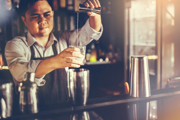 A young bartender is mixing alcohol in a glass to serve customers in a nightclub.