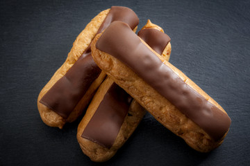 French cuisine and baked desserts concept with whip cream and chocolate eclairs  on a dark black...