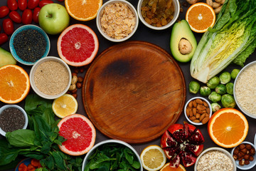 Around wooden kitchen board set clean eating. Vegetarian healthy food - different vegetables and fruits, superfood, seeds, cereal, leaf vegetable on dark background top view Flat lay