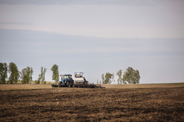 Fototapeta premium a tractor with a trailer plowing field for sowing of agricultural machinery is preparing for a new crop.