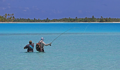 Guide pointing out a fish to fly-fisherman in turquoise waters french polynesia