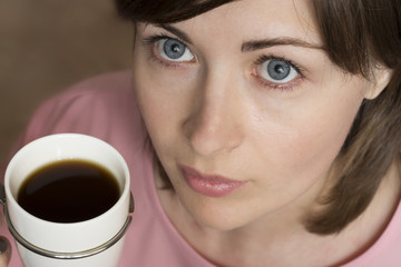 An attractive girl with blue eyes drinks coffee from a white mug. close-up portrait. Top view