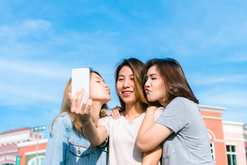Fototapeta na wymiar Group of young Asian Women selfie themselves with a phone in a pastel town after shopping. Young women group do outdoor activity under the blue sky. Outdoor activity after shopping concept.