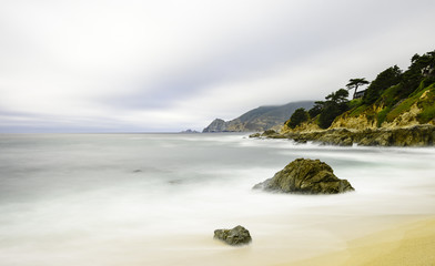 Fototapeta na wymiar foggy flowing California coastline with soft surf and moss covered hills