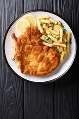 Traditional Italian veal Milanese with lemon and French fries close-up. Vertical top view