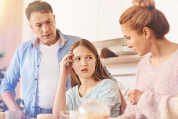 Are you serious. Confused daughter touching her forehead and keeping mouth opened while listening to her parents