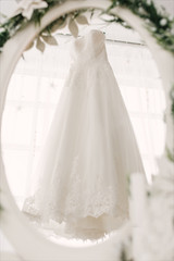 the wedding dress hangs on a hanger and is reflected in the mirror, the bride's morning