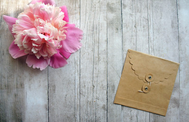 Pink peony with craft envelope on a wooden background, close up, springtime