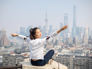 Beautiful young brunette woman sit on top of mansion roof with blur Shanghai Bund landmark buildings background. Emotions, people, beauty and lifestyle concept.