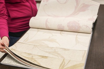 Female hand, choosing the right color from the catalog of wall-papers in the room close-up