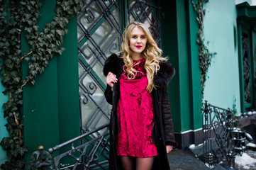 Elegance blonde girl in red evening dress and fur coat at streets of city.