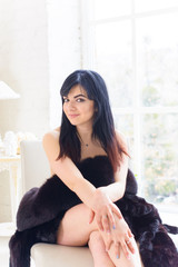 Sexy and tender hispanic american woman in white style interior in bed at the bedroom, dressed in furs. The concept of femininity and attractiveness  