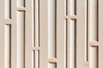 Wall of the building with a relief surface. A pattern of vertical grooves and horizontal partitions. The wall is painted with pink paint. A wall of concrete. The deepening of wide and narrow.