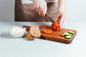 Chef cutting tomatoes on cutting board and preparing fresh healthy organic sandwiches for breakfast