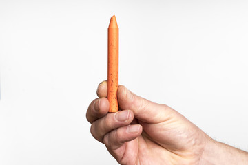 An orange wax crayon in the hand