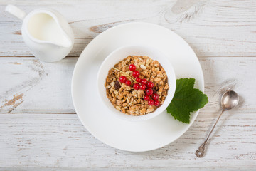 Summer healthy breakfast of granola, muesli with milk jug with red currant decor on light wooden board. Top view.