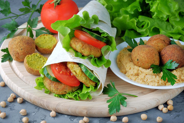 Falafel and vegetables wrapped in lavash and bowl with hummus on cutting board. Traditional arabic food. Close-up view.
