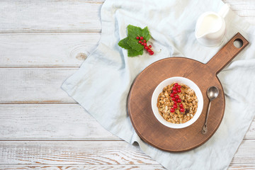 Summer healthy breakfast of granola, muesli with milk jug with red currant decor on wooden board. Top view.