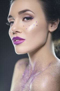Close up beauty portrait of a fantasy art theme: Star Wars cosplay. Princess Leia hairstyle with purple glitters and stars all over woman face and body. Creative violet backlight, studio image
