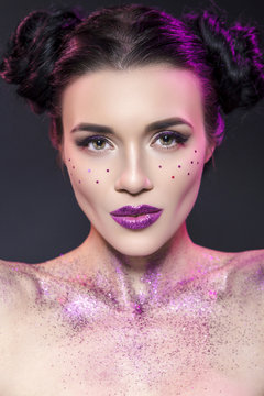 Close up beauty portrait of a fantasy art theme: Star Wars cosplay. Princess Leia hairstyle with purple glitters and stars all over woman face and body. Creative violet backlight, studio image