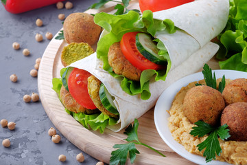 Falafel and vegetables wrapped in lavash and bowl with hummus on  light cutting board. Close-up view.