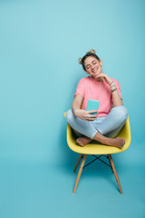 enjoy the music. modern young woman wearing headphones listening to music, sitting on a chair with crossed legs against a blue pastel background