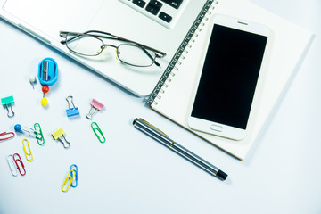 Top view of laptop, blank notebook, paper clips  and smart phone with white background and copy space.