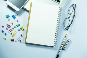 Top view of laptop, blank notebook, paper clips  and smart phone with white background and copy space.