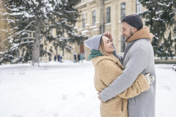 Fototapeta premium Stylish caucasian couple of man and woman waling in the european city park in winter. Cold, snowy day. Space for text