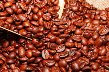 A wooden scoop is pouring grains of coffee into a bag