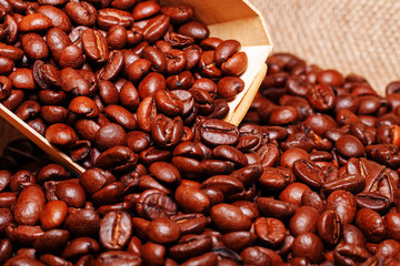 A wooden scoop is pouring grains of coffee into a bag