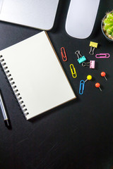 Top view of office table or desk with blank notebook, laptop, colorful equipment and smart phone on black background with copy space for text.