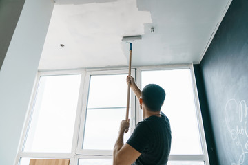 the man paints the walls and the ceiling in gray color, standing with his back to the camera. Focus...