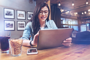 Modern igeneration. Happy attractive young woman sitting at the table and using a tablet while being at the bar