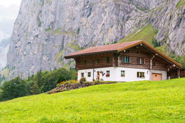 Alpine house in Lauterbrunnen under rock and green grass in front off. 