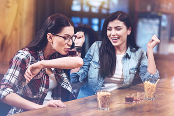 Drink it. Joyful pretty nice woman looking at her friend and cheering her up while having a great time in the bar