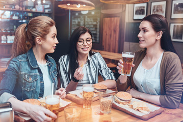 Friends chat. Positive pretty young women drinking beer and eating food while having a conversation
