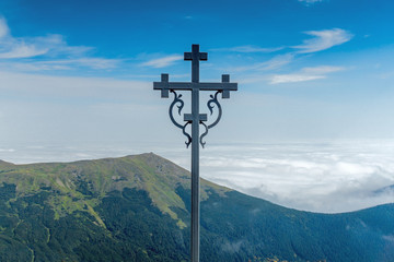 Landscape of mountain chain in a clouds and cross on foreground. Carpathian Mountains in a summer sunny day.