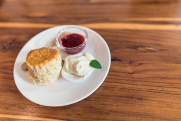Scone with jam , clotted cream on whit plate on wooden table