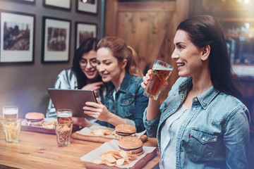 Alcoholic drink. Positive happy nice woman holding a glass and drinking beer while having a great time with her friends
