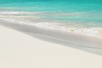 Fototapeta na wymiar A small wave of ocean foams on the sandy Caribbean beach.