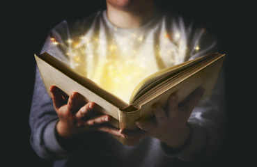 Woman holding an open book bursting with light.