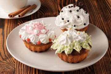 Three homemade baked cupcakes on a white plate placed on a wooden table.