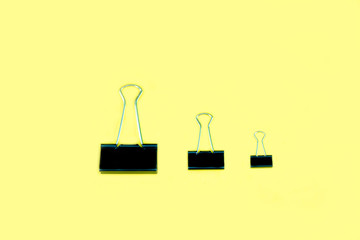 Fototapeta na wymiar Three size for black and metallic binder clip on yellow background.