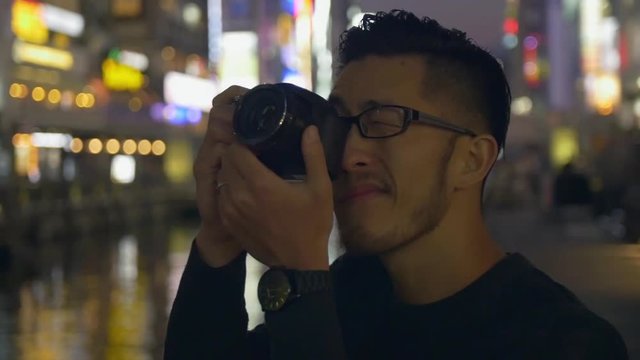 Asian tourist taking photos of city lights with camera.