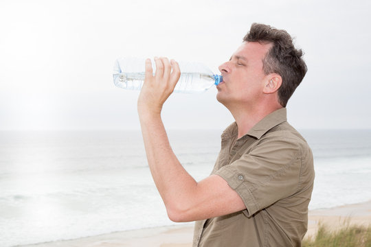 man is drinking water from a plastic bottle against the sky on sea beach